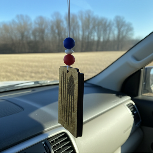 Wooden car freshener with a tattered American flag hanging from the rearview mirror with red, white and blue beads