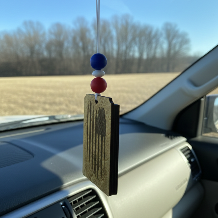 Wooden car freshener with a tattered American flag hanging from the rearview mirror with red, white and blue beads
