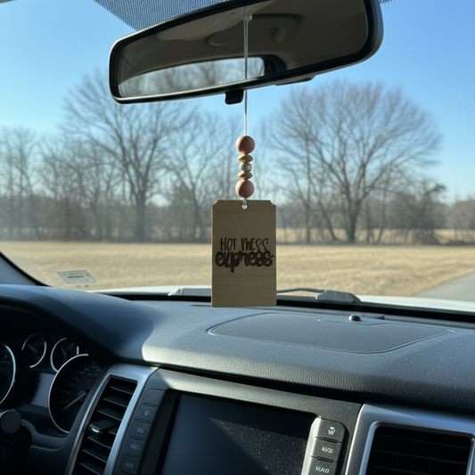 Wooden car freshener that says hot mess express with light pink beads hanging from a rearview mirror