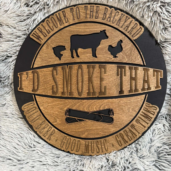 Round sign laser engraved and cut that says I'd Smoke that and has chicken cow fish and cigars. Welcome to the back yard, cold beer, good music, great times