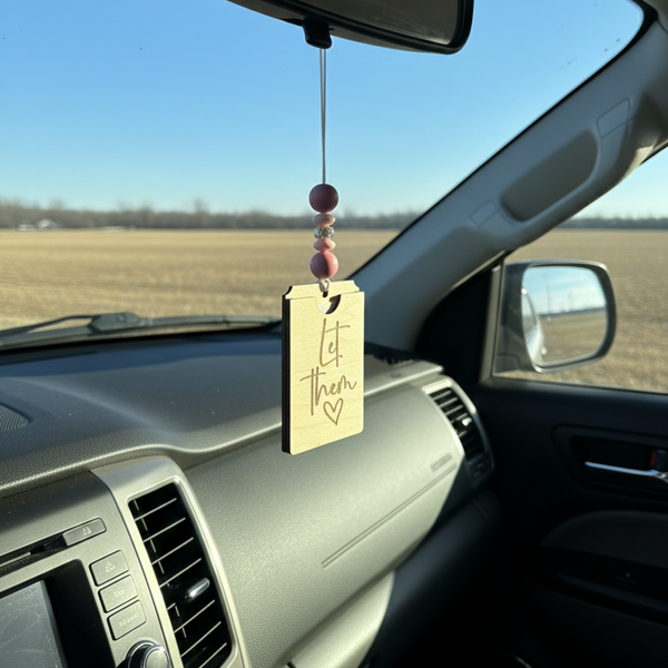 wooden car freshener hanging from a rearview mirror with the phrase engraved 