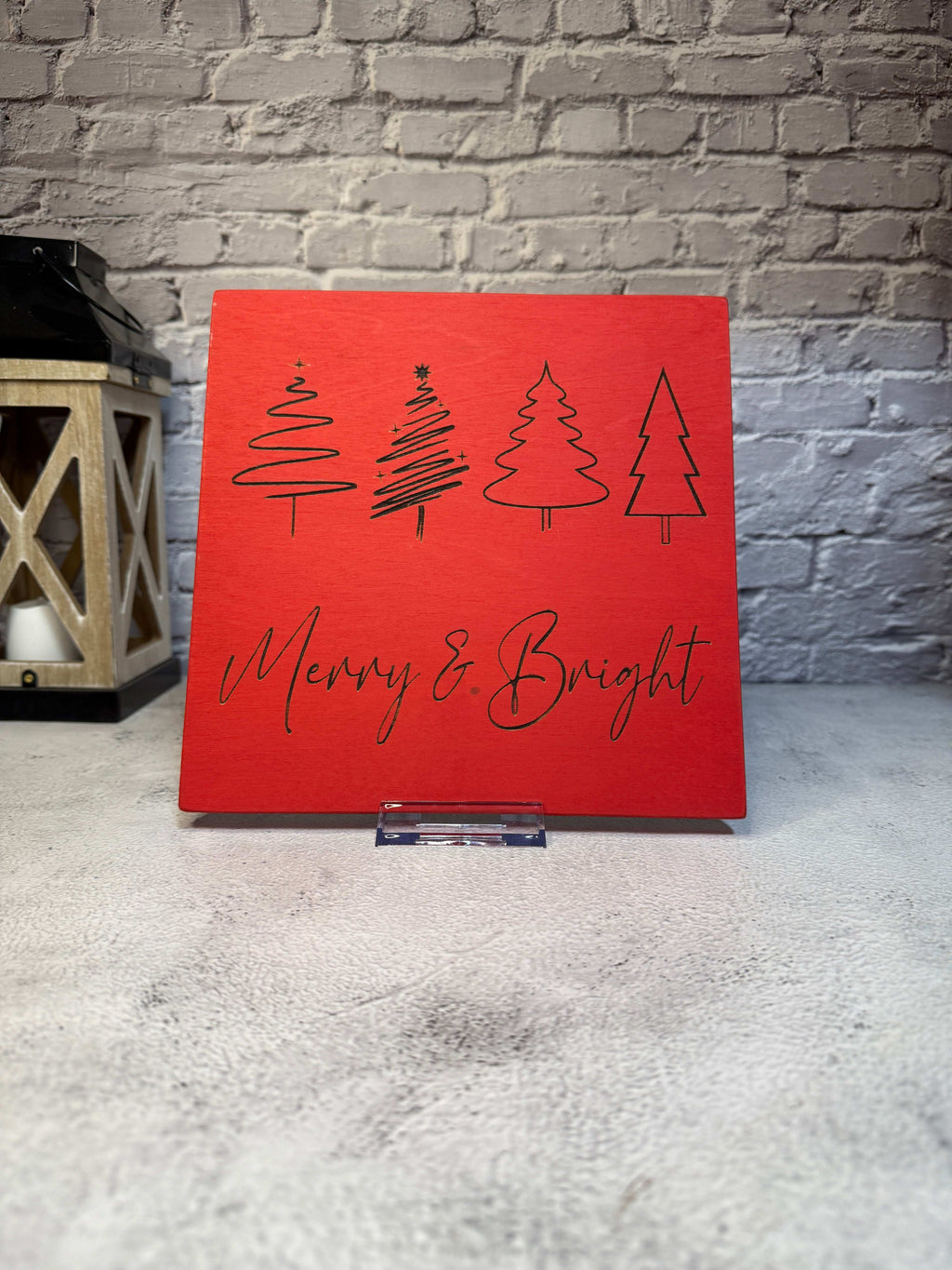 Red sign with Christmas tree designs and 'Merry & Bright' text against a textured wall. 