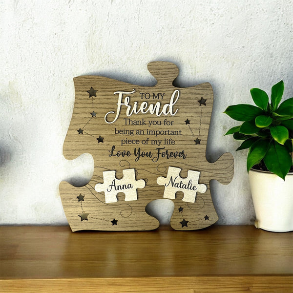 Wooden puzzle piece to my friend thank you for being an important piece of my life love you forever with engraved message and names on a wooden surface with a plant in the background.