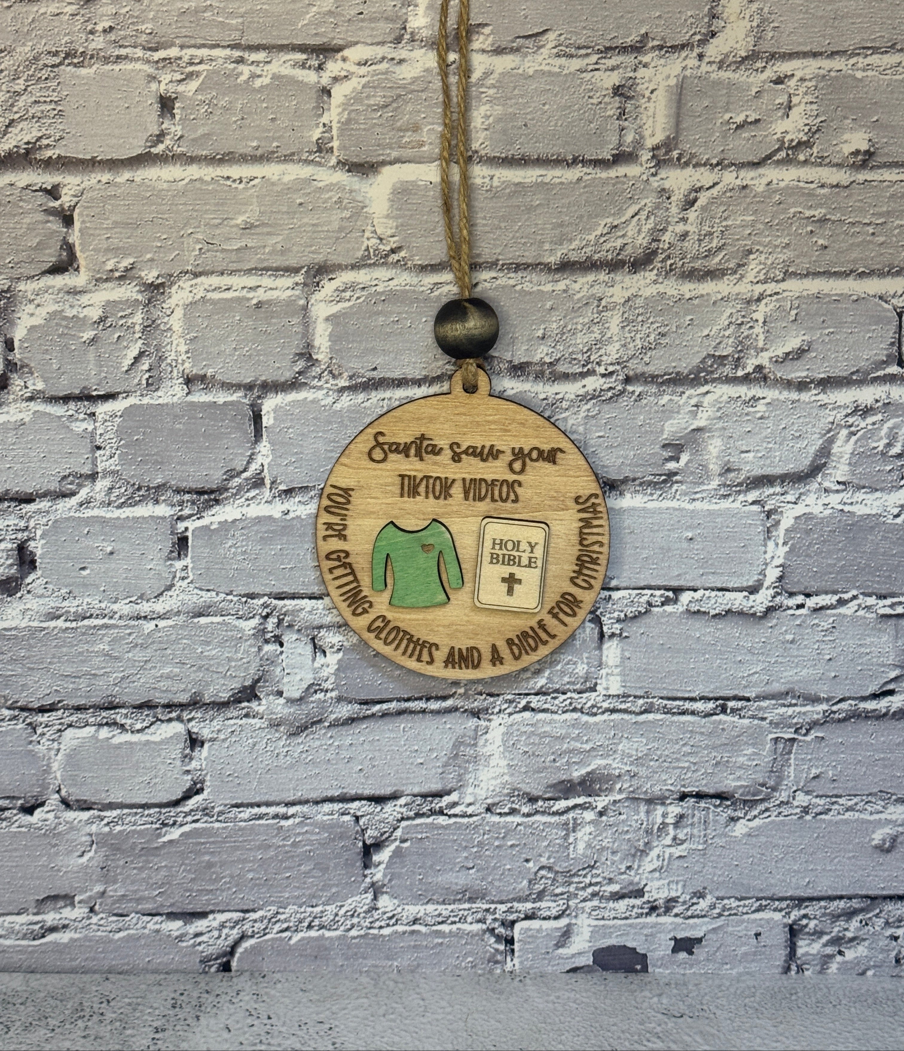 Wooden TikTok Ornament against a brick wall with a shirt and bible