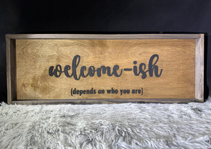 Wooden framed sign with 'welcome-ish (depends on who you are)' text on a textured surface