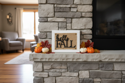 A burlap and wood sign reading 'hello FALL' in black script and block lettering, displayed on a stone fireplace mantel with small pumpkins, fall leaves, and a warm living room in the background.