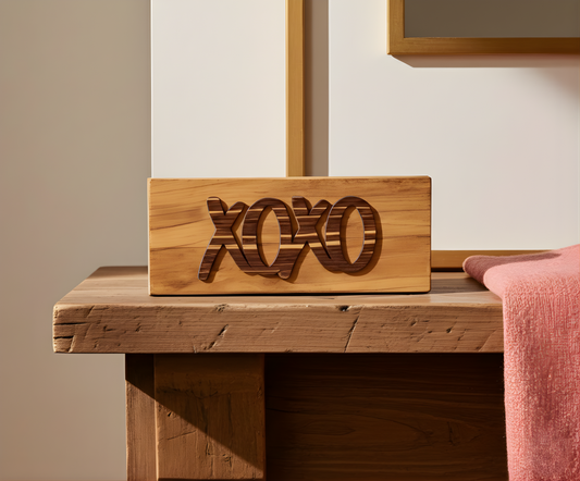 wood sign with the word xoxo sitting on a wood desk with a light red towel beside it.